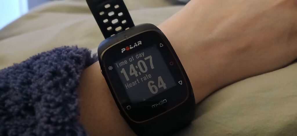 Photo d'une montre de sport sur un poignet. Affichage de l'heure et de la fréquence cardiaque en gros chiffres sur l'écran. 